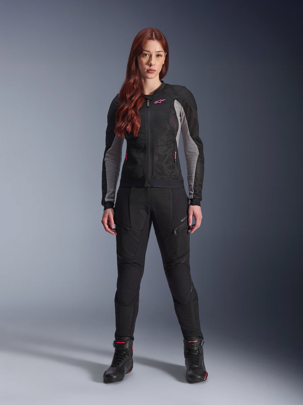 Alpinestars Stella Troop-Air Hose, Damen-Motorradhose in Schwarz, mit Mesh-Einsätzen und Reißverschlusstaschen, kombiniert mit einer passenden schwarz-grauen Mesh-Jacke mit pinken Akzenten und schwarzen Motorradstiefeln, komplettes urbanes Motorrad-Outfit.