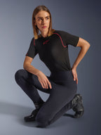 Alpinestars Stella Flex-Ast Leggings, Schwarz, getragen von einer knienden Frau in einer Studioumgebung, kombiniert mit einem schwarzen, kurzärmeligen Performance-Oberteil mit rosa Besatz und schwarzen Motorradstiefeln, mit hoher Taille und flexiblen Einsätzen für urbanes Fahren.