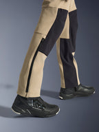 Alpinestars Stella Flex-AST Explorer Damenhose, Motorrad-Abenteuerhose, Sand und Schwarz, Nahaufnahme der Unterschenkel und Knöchel mit langem seitlichem Reißverschluss und schwarzen Verstärkungspanelen, getragen mit schwarzen Alpinestars Motorradschuhen.