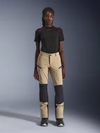 Alpinestars Stella Flex-AST Explorer Hose für Damen, Motorradhose, Beige mit schwarzen Einsätzen, getragen von einem Modell mit schwarzem Kurzarm-Oberteil und schwarzen Stiefeln, mit verstärkten Kniepartien, Cargotaschen mit Reißverschluss und atmungsaktivem Ripstop-Gewebe für Adventure-Fahrten bei warmem Wetter.