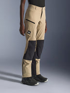 Frau trägt Alpinestars Stella Flex-AST Explorer Hose, sandfarbene und schwarze Adventure-Motorradhose mit schwarzen Ripstop-Knieeinsätzen, Cargo-Taschen mit Reißverschluss, 'ALL TERRA' Logo-Patch und Reißverschlüssen am Beinabschluss.