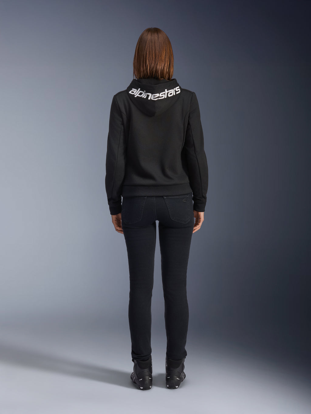 Daisy V3 Damen-Motorrad-Jeans, Black Rinse, Slim-Fit Motorradhose, Rückansicht mit hohem Bund und femininer Silhouette, kombiniert mit einem schwarzen Alpinestars-Hoodie und schwarzen Motorradstiefeln, urbane Casual-Fahrerausrüstung