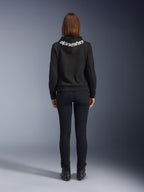 Daisy V3 Damen-Motorrad-Jeans, Black Rinse, Slim-Fit Motorradhose, Rückansicht mit hohem Bund und femininer Silhouette, kombiniert mit einem schwarzen Alpinestars-Hoodie und schwarzen Motorradstiefeln, urbane Casual-Fahrerausrüstung
