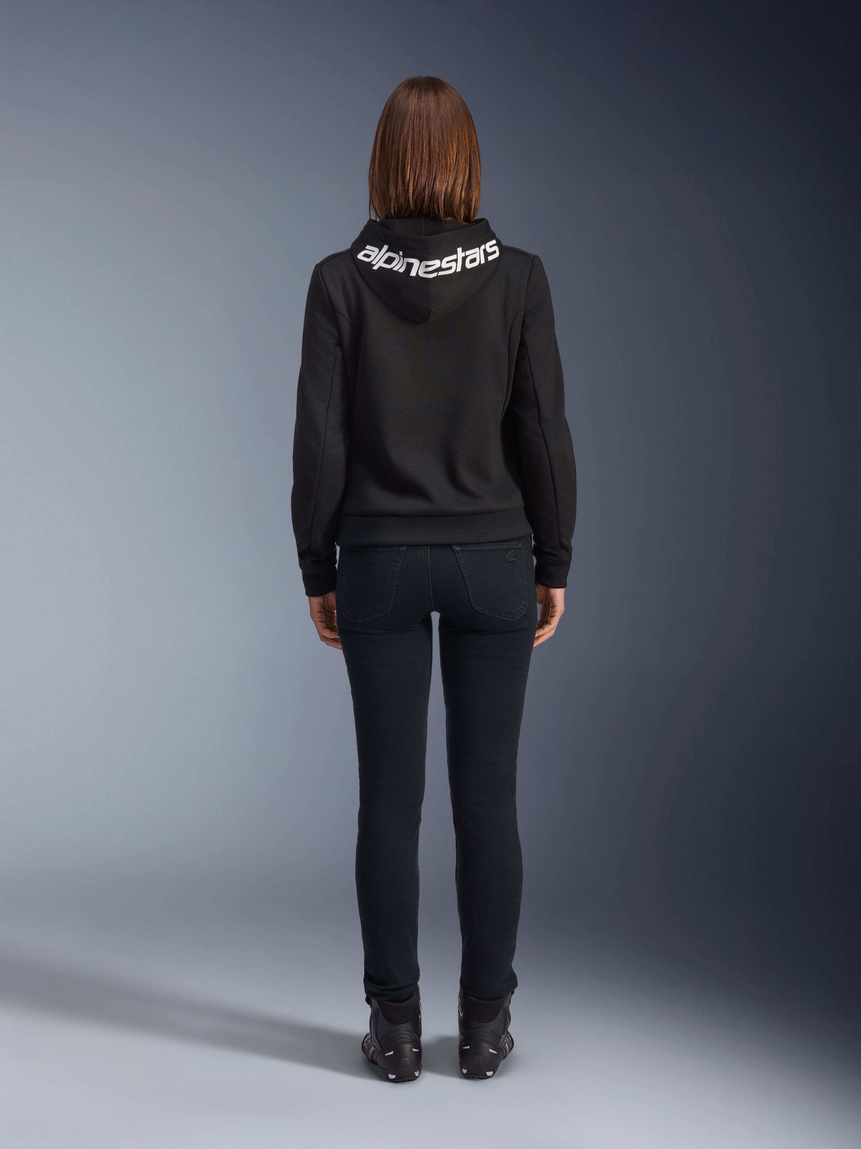 Daisy V3 Damen-Motorrad-Jeans, Black Rinse, Slim-Fit Motorradhose, Rückansicht mit hohem Bund und femininer Silhouette, kombiniert mit einem schwarzen Alpinestars-Hoodie und schwarzen Motorradstiefeln, urbane Casual-Fahrerausrüstung