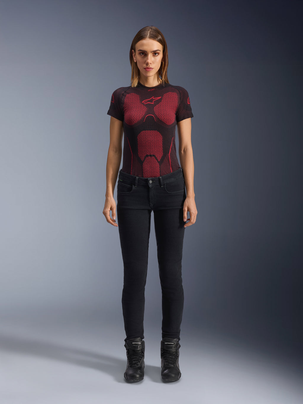 Alpinestars Daisy V3 Damen-Motorradjeans, Rinse Black, Slim-Fit Motorradhose, getragen von einem Model mit einem rot-schwarz gemusterten technischen T-Shirt und schwarzen Motorradstiefeln, lässige urbane Fahrausrüstung mit femininer Silhouette und High-Waist-Design.
