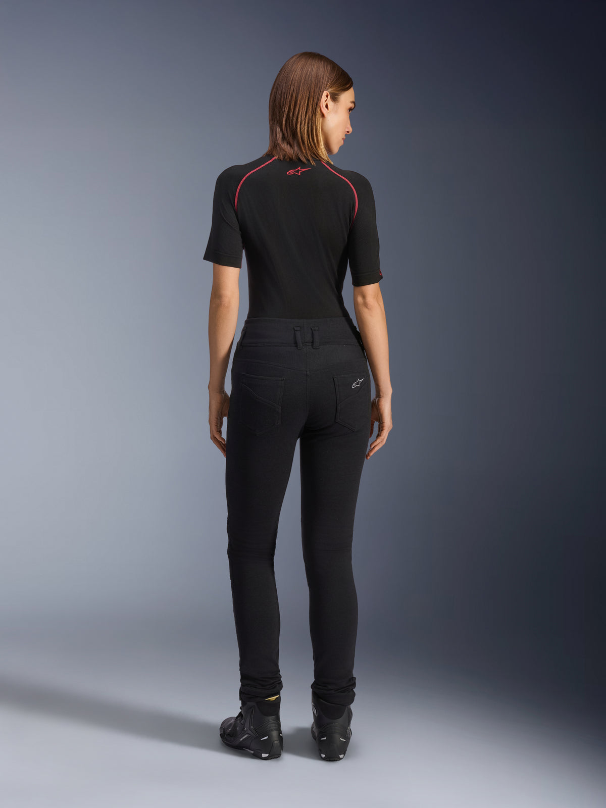 Alpinestars Damen Banshee Leggings, schwarze Motorrad-Leggings, Rückansicht zeigt figurbetonte Passform und anatomisches Stretch-Gewebe, mit Gesäßtaschen und Logo-Detail, getragen mit schwarzem Baselayer und Motorradschuhen, urbane Motorradbekleidung für Damen