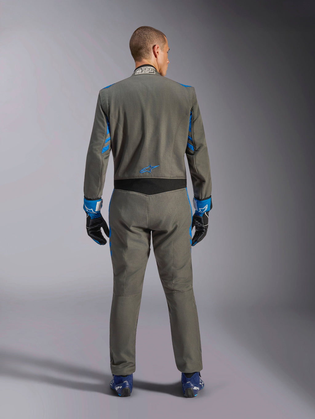 Alpinestars GP Race V3 Anzug FIA, Rückansicht, Anthrazit-Blau mit leuchtend blauen Details an Armen und Schultern, mit blauem Stern-Logo auf dem unteren Rücken, getragen mit passenden Rennhandschuhen und blauen Schuhen, professioneller Auto-Rennanzug