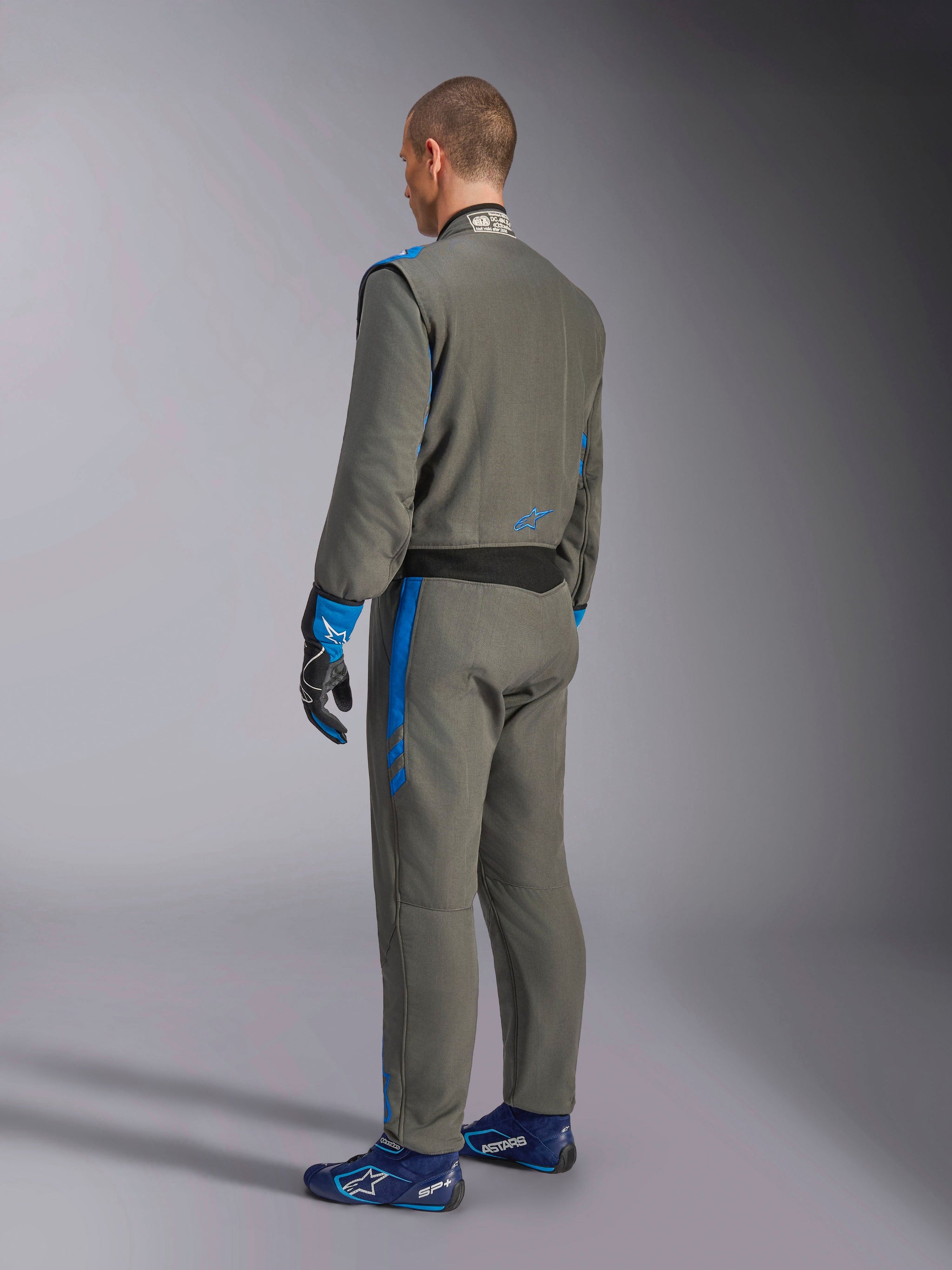 Alpinestars GP Race V3 Suit FIA, Auto-Rennanzug, Anthrazit-Blau, Rückansicht eines Modells im grauen einteiligen Anzug mit blauen Akzenten, passenden blauen Handschuhen und Rennschuhen, professionelles Motorsport-Design