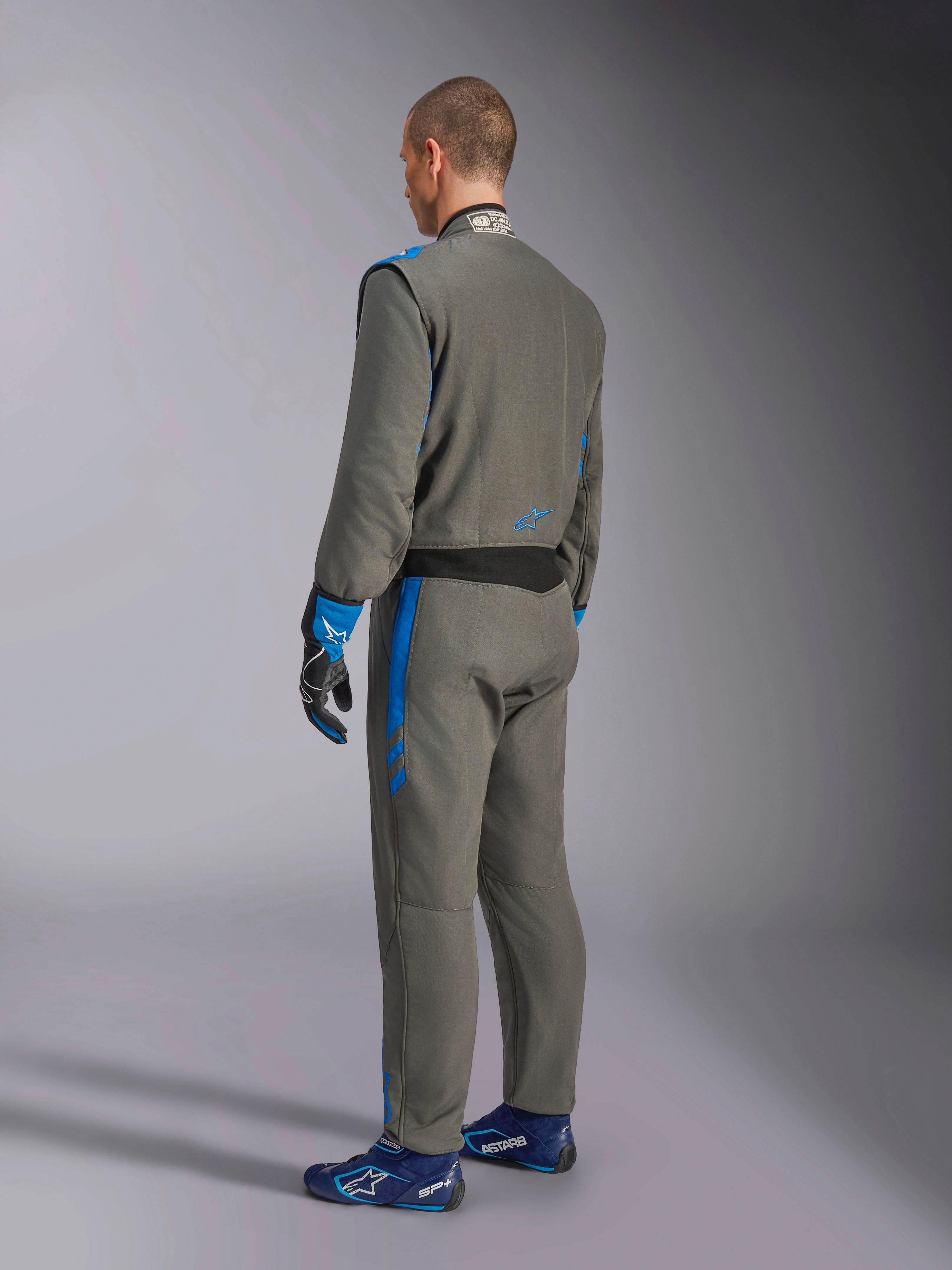Alpinestars GP Race V3 Suit FIA, Auto-Rennanzug, Anthrazit-Blau, Rückansicht eines Modells im grauen einteiligen Anzug mit blauen Akzenten, passenden blauen Handschuhen und Rennschuhen, professionelles Motorsport-Design