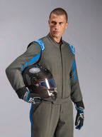 Männlicher Rennfahrer im Alpinestars GP Race V3 Anzug FIA in Anthrazit-Blau, hält einen Carbon-Rennhelm mit schillerndem Visier, professionelle Autorenn-Ausrüstung mit blauen Schulterakzenten und passenden Rennhandschuhen.