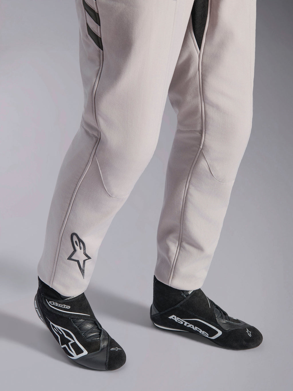 Alpinestars GP Race V3 Anzug FIA, Automobil-Rennanzug in Silver Anthracite, Detailaufnahme der Unterschenkel und schwarzen Rennstiefel, mit dem schwarzen Astars-Logo auf der Wade, professionelle Motorsportausrüstung mit Rippbündchen