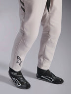 Alpinestars GP Race V3 Anzug FIA, Automobil-Rennanzug in Silver Anthracite, Detailaufnahme der Unterschenkel und schwarzen Rennstiefel, mit dem schwarzen Astars-Logo auf der Wade, professionelle Motorsportausrüstung mit Rippbündchen