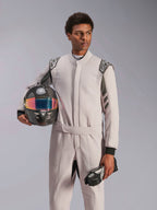 Alpinestars GP Race V3 Anzug FIA, Autorennanzug, Silber Anthrazit, getragen von Model mit Carbonhelm mit irisierendem Visier und schwarzen Rennhandschuhen, professionelle Motorsport-Schutzausrüstung mit sichtbaren Schulter-Epauletten.