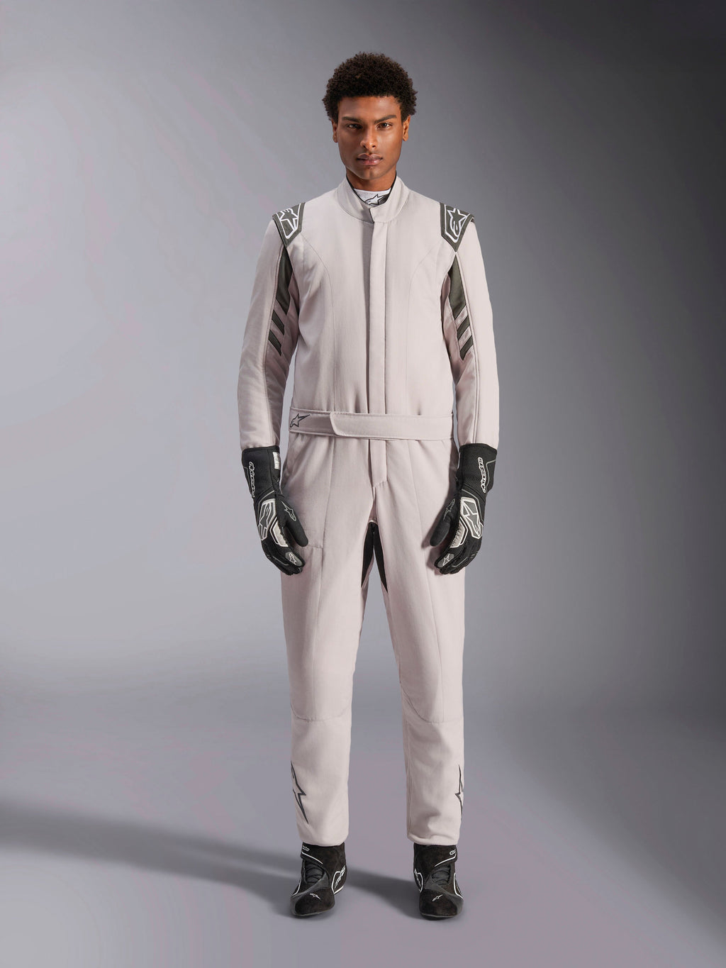 Alpinestars GP Race V3 Anzug FIA in Silber Anthrazit, einteiliger Autorennanzug, von einem Model getragen, mit dunkelgrauen Schulterklappen und Akzenten, kombiniert mit schwarzen Rennhandschuhen und Stiefeln, professionelle Motorsport-Schutzausrüstung