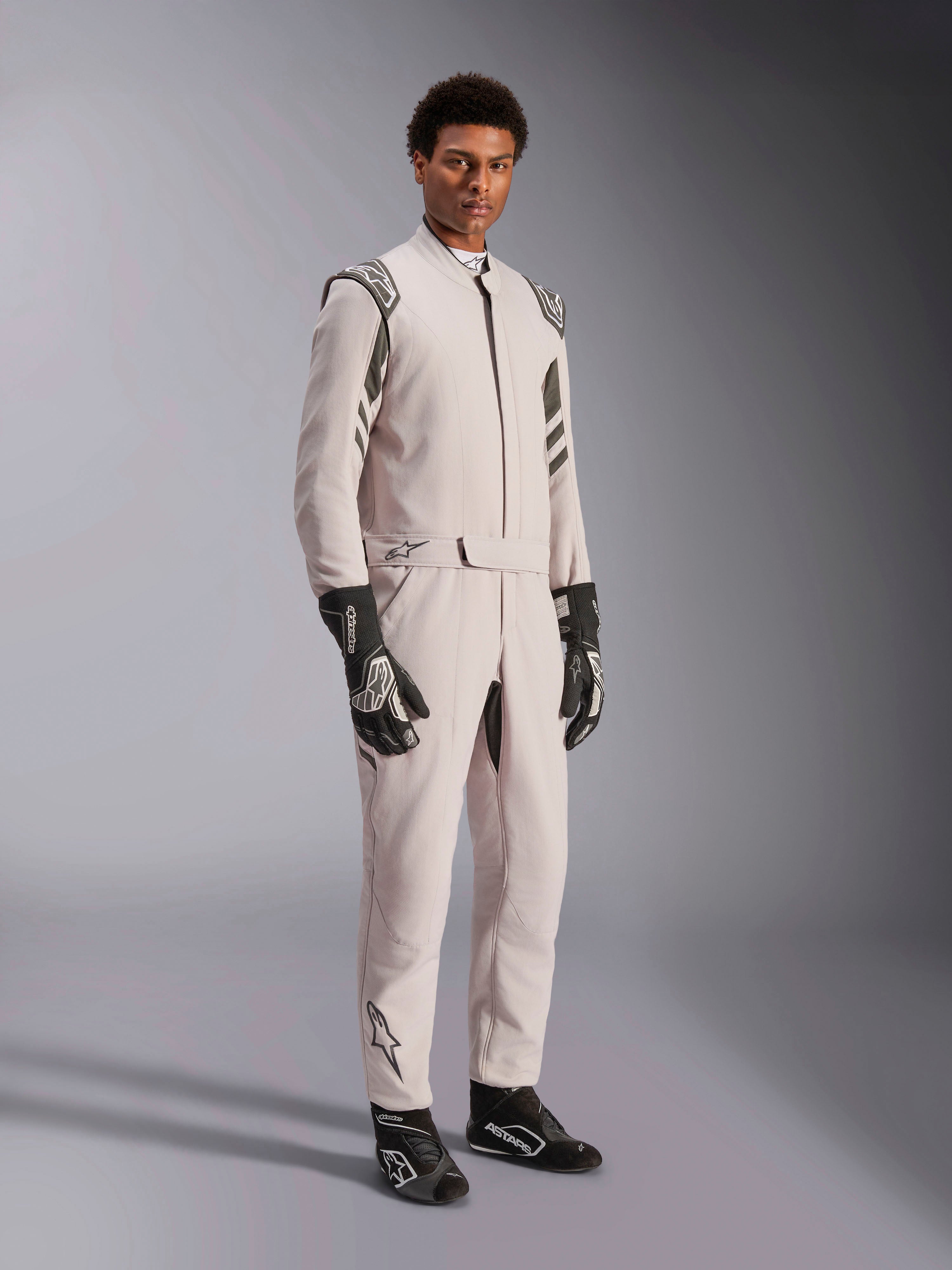 Alpinestars GP Race V3 Anzug FIA, Rennanzug in Silver Anthracite, einteiliger Fahreranzug mit Schulter-Epauletten und Gürtelbund, getragen mit passenden schwarz-weißen Rennhandschuhen und Stiefeln, elegantes Design für den professionellen Autorennsport