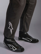 Alpinestars GP Race V3 FIA Anzug, Nahaufnahme der Unterschenkel und Rennstiefel, Schwarz mit silbernen Akzenten, weiß besticktes Stern-Logo auf dem Schienbein, gerippte Knöchelbündchen, professionelle Automobil-Rennsport-Schutzausrüstung