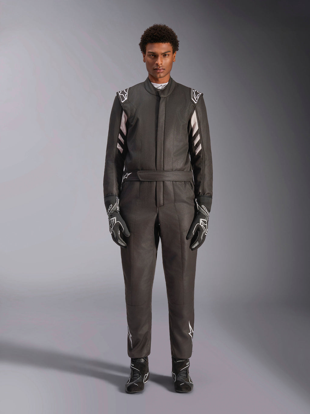 Alpinestars GP Race V3 Anzug FIA, Auto-Rennanzug, Schwarz und Silber, Vorderansicht eines Fahrers in vollständiger Rennausrüstung inklusive Handschuhen und Stiefeln, professionelles Motorsport-Design mit Alpinestars-Branding an den Schultern und am Gürtel