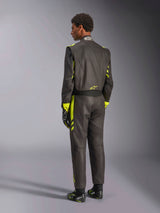 Rear view of the Alpinestars GP Race V3 Suit FIA, black with yellow fluo accents, worn with matching racing gloves and boots, professional auto racing gear featuring a two-layer aramidic construction