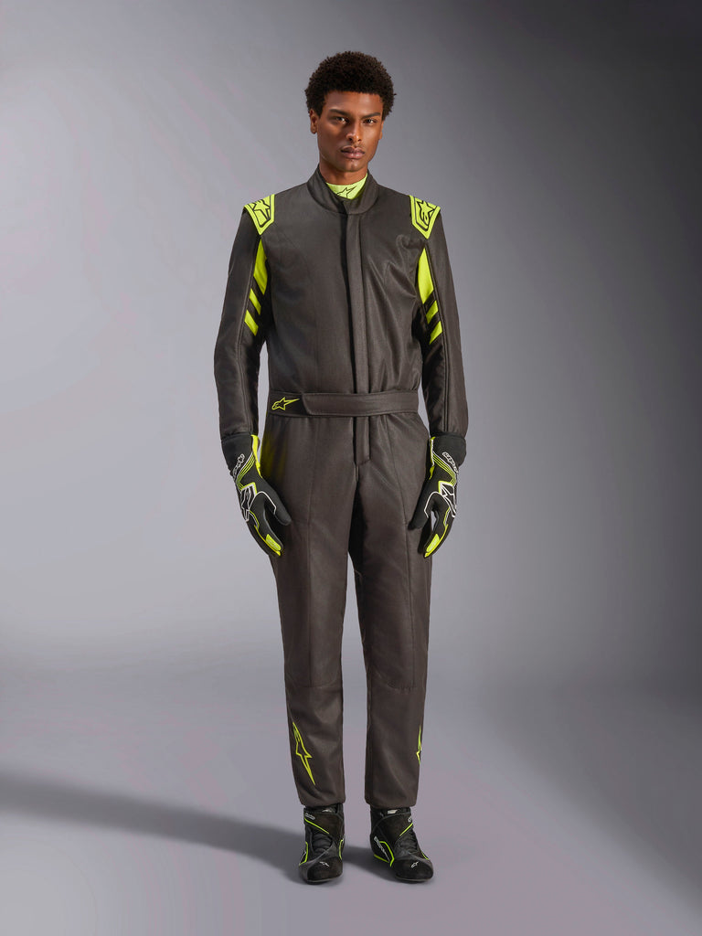 Alpinestars GP Race V3 Anzug FIA, Autorennanzug, Schwarz und Gelb Fluo, von einem Modell getragen mit passenden Rennhandschuhen und Stiefeln, leuchtend gelbe Akzente an Schultern, Taille und Ärmeln, professionelle Motorsportausrüstung