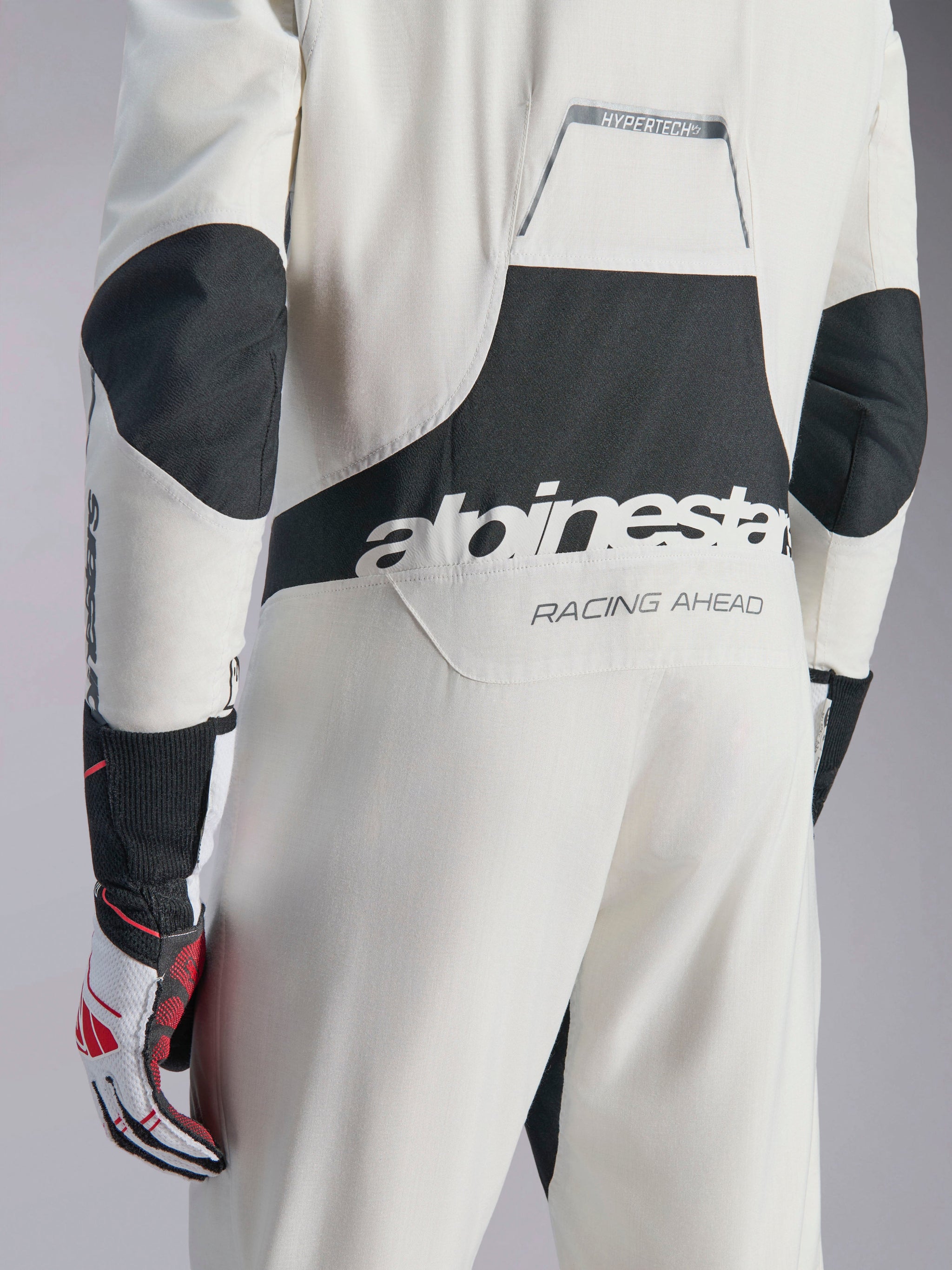 Alpinestars Hypertech V3 Suit, White Black and Silver auto racing suit, back view showing large black 'alpinestars' logo and 'RACING AHEAD' text, featuring black stretch panels on the elbows and lumbar area, professional motorsport protective clothing.