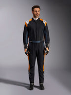Alpinestars GP Pro Comp V2 FIA Rennanzug, Autorennanzug in Schwarz Asphalt und Orange Fluo, männliches Model in vollständiger Schutzausrüstung mit passenden Rennhandschuhen und Schuhen, weiße Alpinestars-Logos und leuchtend orangefarbene Seitenpaneele, professionelle Motorsport-Bekleidung