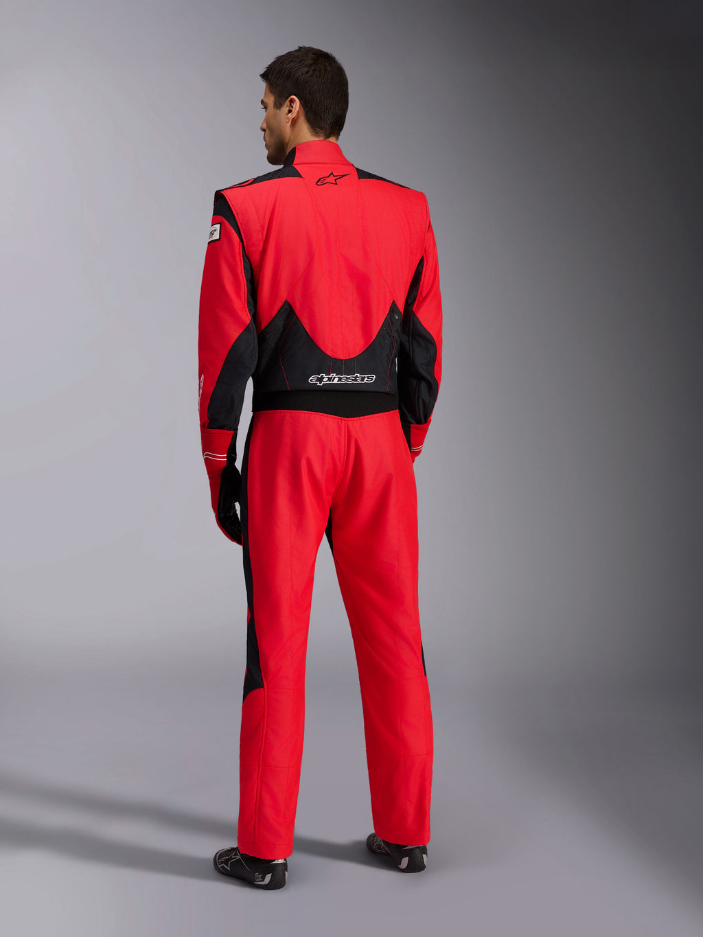 Vollständige Rückansicht des Alpinestars GP Pro Comp V2 FIA Rennanzugs, Rot und Schwarz, mit atmungsaktiven schwarzen Mesh-Einsätzen an Schultern und unterem Rücken, weißem Alpinestars-Logo, getragen mit passenden Rennhandschuhen und Stiefeln, professionelle Motorsport-Ausrüstung