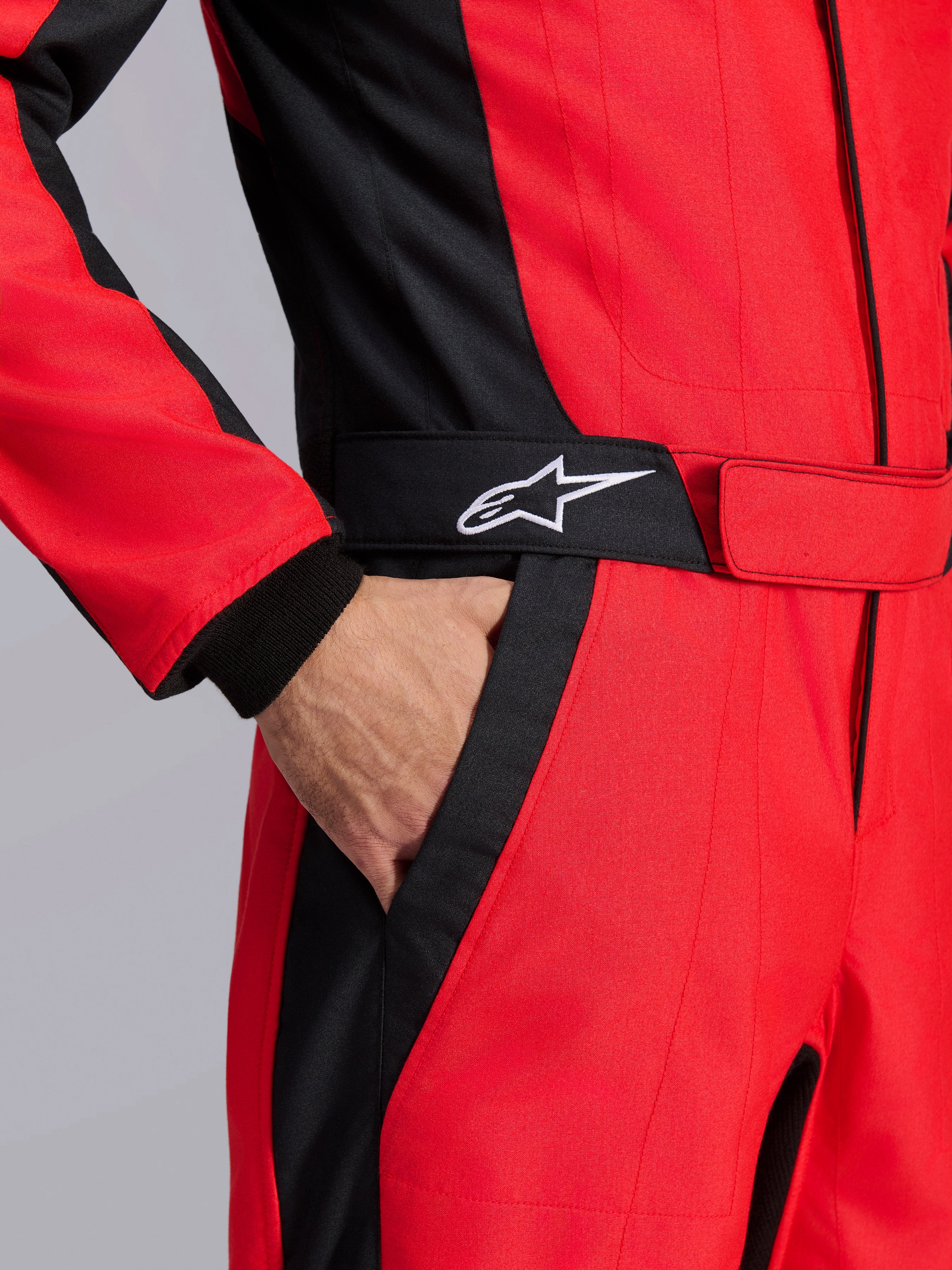 Alpinestars GP Pro Comp V2 FIA Rennanzug, Rot und Schwarz, Nahaufnahme des Taillenbereichs mit einer Hand in der Tasche, schwarzer Gürtel mit weißem Stern-Logo, strukturierte Einsätze für den Autorennsport