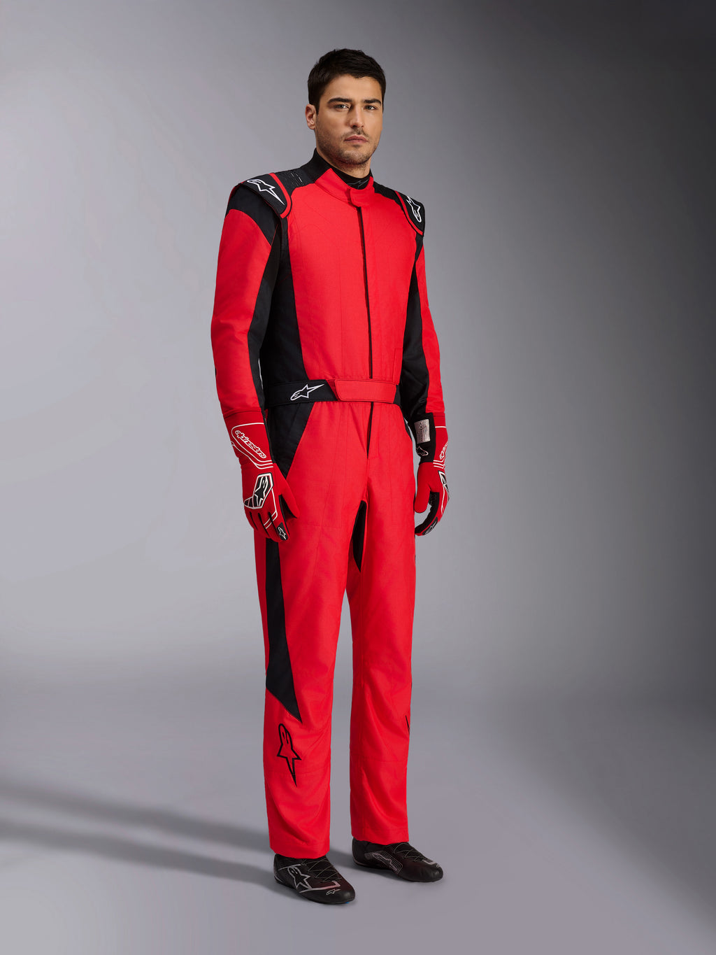 Alpinestars GP Pro Comp V2 FIA Rennanzug, professioneller Auto-Rennanzug in Rot und Schwarz, getragen mit passenden rot-weißen Handschuhen und schwarzen Rennschuhen, Ganzkörper-Studioporträt von Motorsport-Schutzausrüstung.