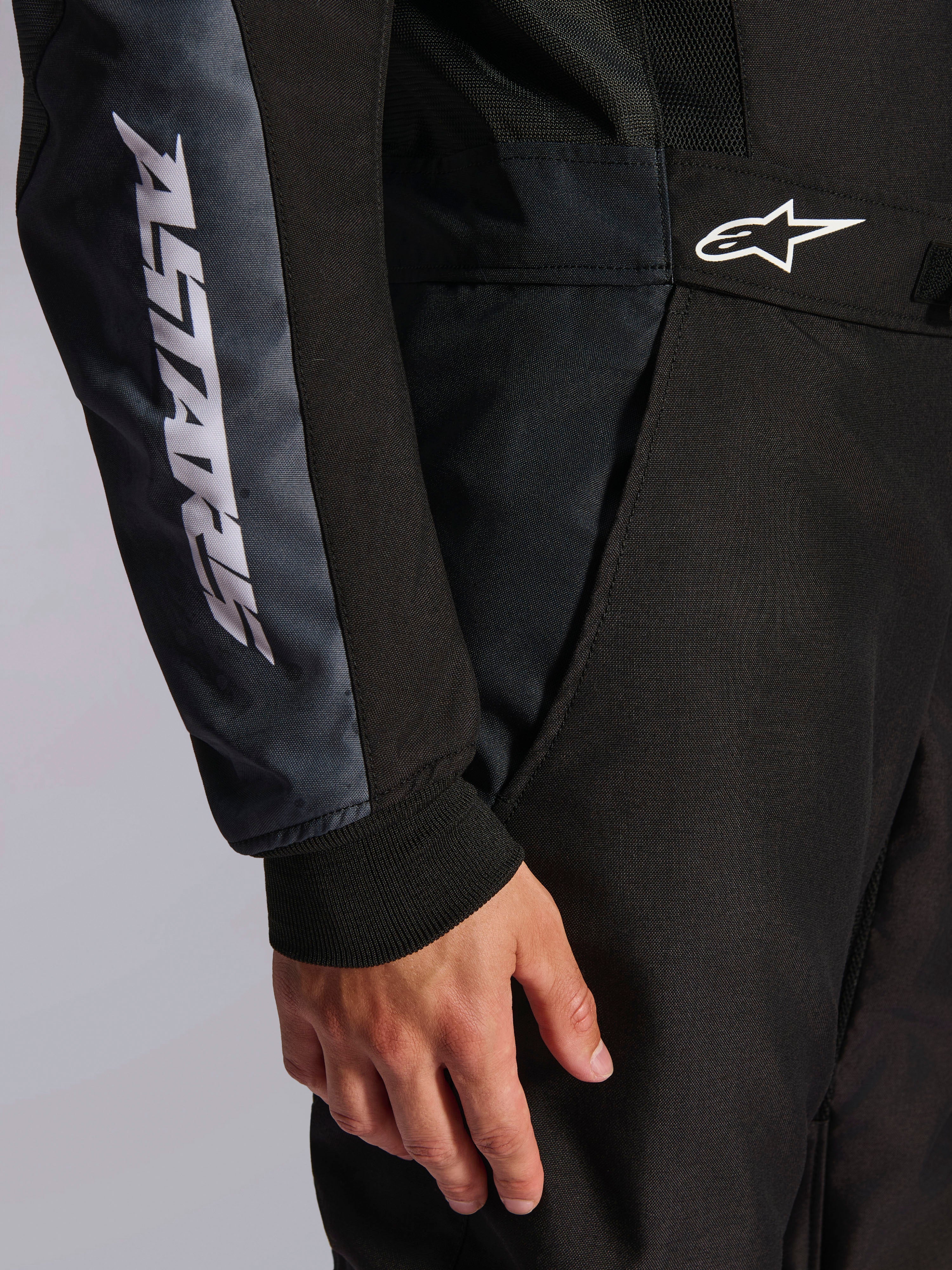 Alpinestars KMX-5 V3 Anzug, Kart-Anzug, Schwarz und Dark Shadow, Nahaufnahme von Hüfte und Arm, weißes ASTARS-Branding am Ärmel, weißes Logo an der Taille, Mesh-Einsätze zur Belüftung und gestricktes Ärmelbündchen