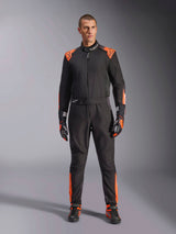 Alpinestars KMX-5 V3 Suit, Black and Orange Fluo karting suit, worn by a model with matching racing gloves and shoes, featuring orange accents on the shoulders and legs, professional one-piece motorsport design with a technical mesh appearance.