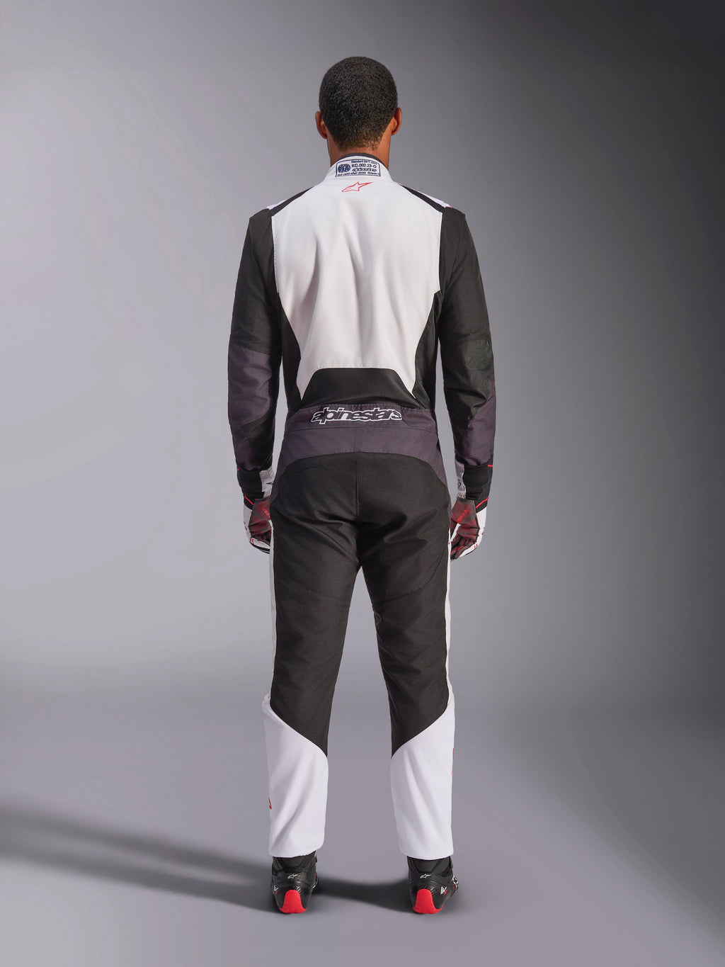 Alpinestars KMX-5 V3 Anzug, Kart-Anzug, Weiß, Schwarz und leuchtendes Rot, Rückansicht, einteiliger Rennanzug mit atmungsaktiven Mesh-Einsätzen und Alpinestars-Logo an der Taille, getragen mit passenden Rennhandschuhen und Stiefeln