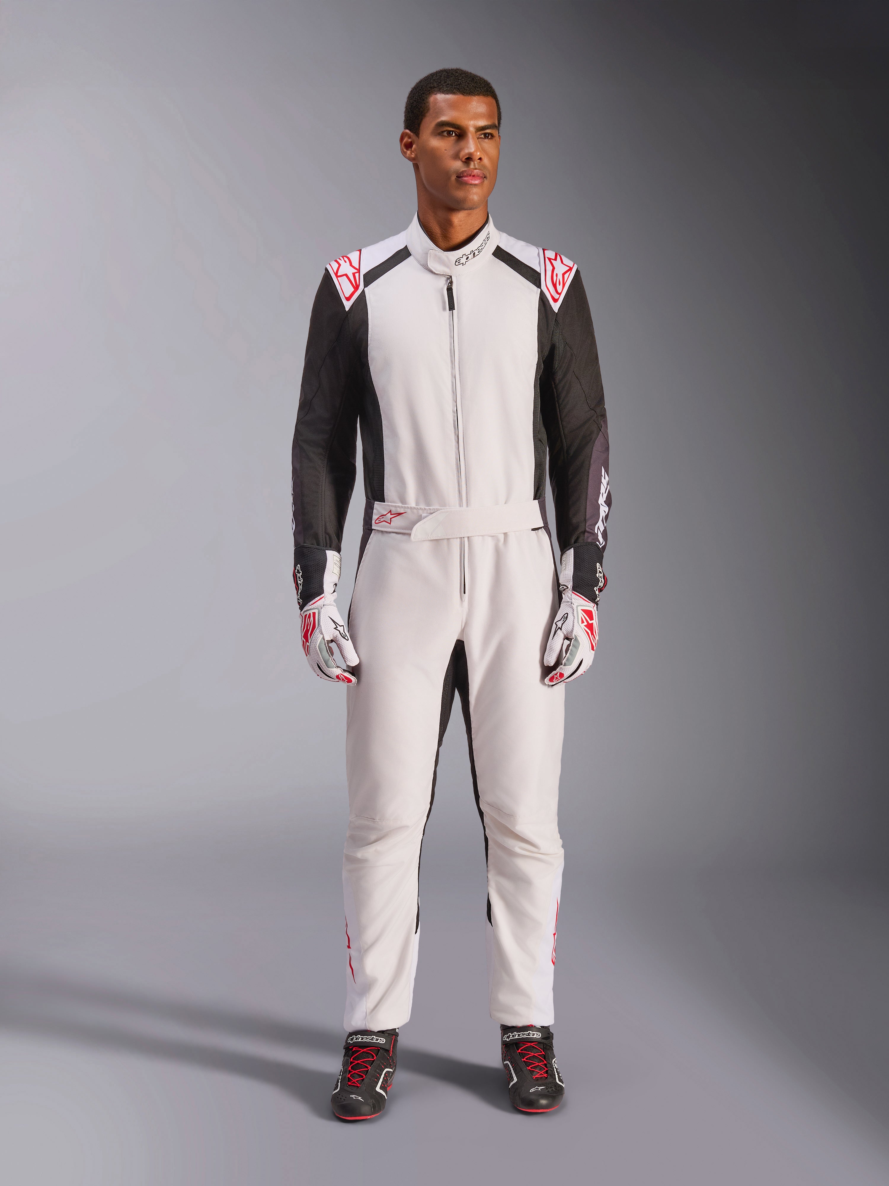 Alpinestars KMX-5 V3 Anzug, einteiliger Kart-Anzug, Weiß, Schwarz und leuchtendes Rot, getragen von einem Model mit passenden Rennhandschuhen und Schuhen, professionelle Motorsportausrüstung für den kompetitiven Kartsport