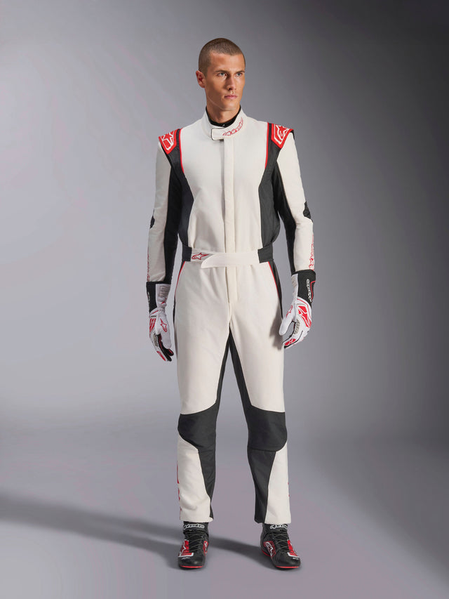 Alpinestars GP Tech V4 Suit, White Black and Red one-piece auto racing suit, worn by a male model with matching racing gloves and shoes, featuring red logos on the shoulders and black side panels, professional motorsport gear for track use.