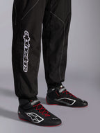 Alpinestars KMX-9 V3 Anzug, Kart-Anzug, Schwarz und Weiß, Detailansicht der Unterschenkel mit großem weißem Alpinestars-Branding, getragen mit schwarz-roten Rennstiefeln, professionelle Motorsport-Ausrüstung für den Kartsport