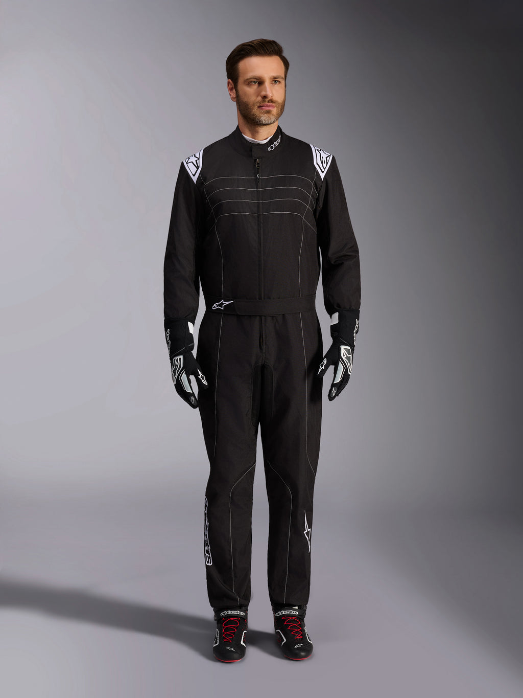Alpinestars KMX-9 V3 Anzug, schwarz-weißer Kart-Anzug, Ganzkörperansicht an einem Modell, mit weißen Schulterlogos und Akzenten, kombiniert mit schwarz-weißen Rennhandschuhen und schwarzen Schuhen mit roten Schnürsenkeln, sportlich-reguläre Passform für professionelle Kart-Ausrüstung.