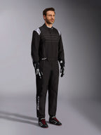 Alpinestars KMX-9 V3 Karting-Anzug, Schwarz und Weiß, männliches Model in vollständigem Rennanzug mit weißem Alpinestars-Logo auf den Epauletten, kombiniert mit schwarz-weißen Rennhandschuhen und schwarzen Kart-Schuhen mit roten Schnürsenkeln, Studioaufnahme zeigt Front- und Seitenprofil