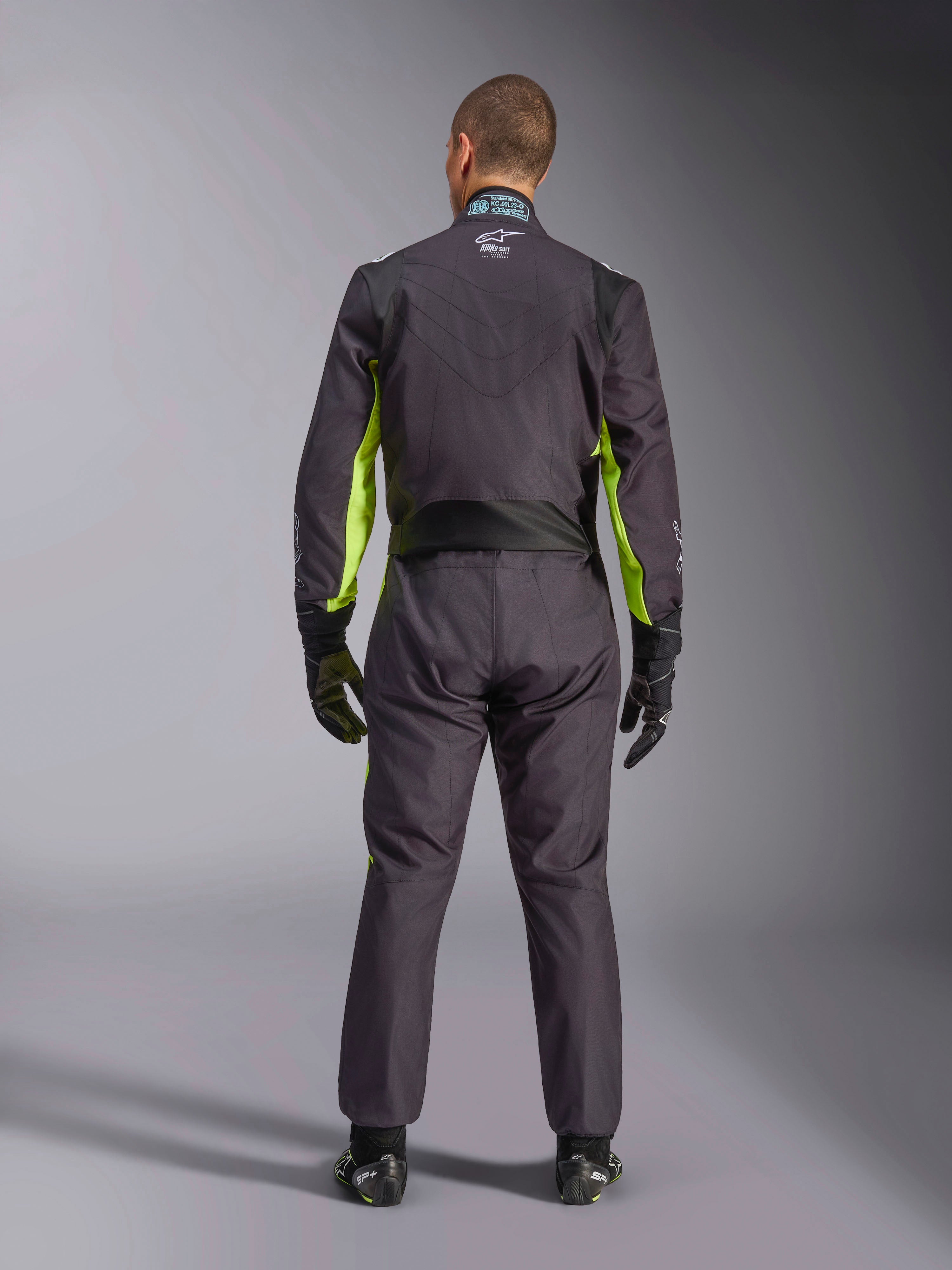 Full-body rear view of a person wearing the Alpinestars KMX-9 V3 Graphic 3 Suit, Karting Suit in Black and Yellow Fluo, showing ergonomic stretch panels on the back and shoulders, paired with black racing gloves and footwear.