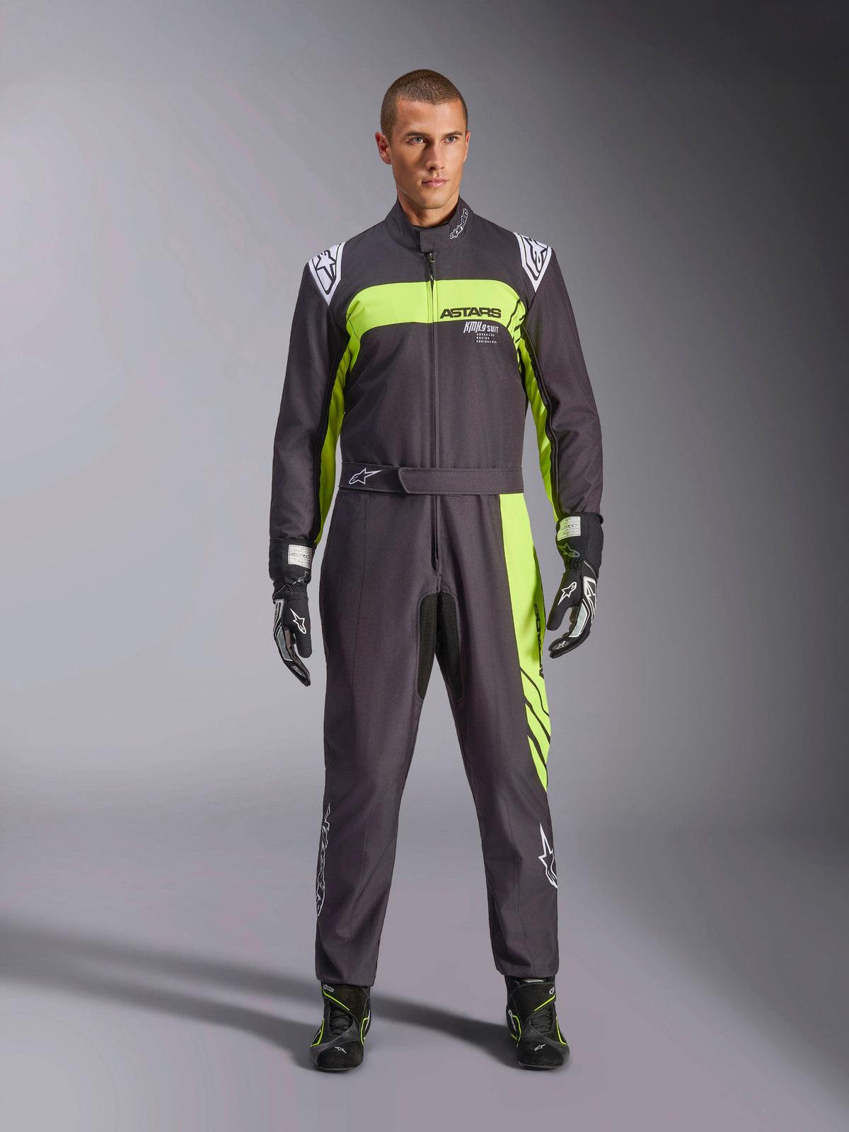 Alpinestars KMX-9 V3 Graphic 3 Anzug, Schwarz und Gelb Fluo, professioneller einteiliger Kart-Anzug getragen von einem Model, mit markanten neongelben Akzenten, ASTARS-Branding auf der Brust sowie passenden Rennhandschuhen und Stiefeln.