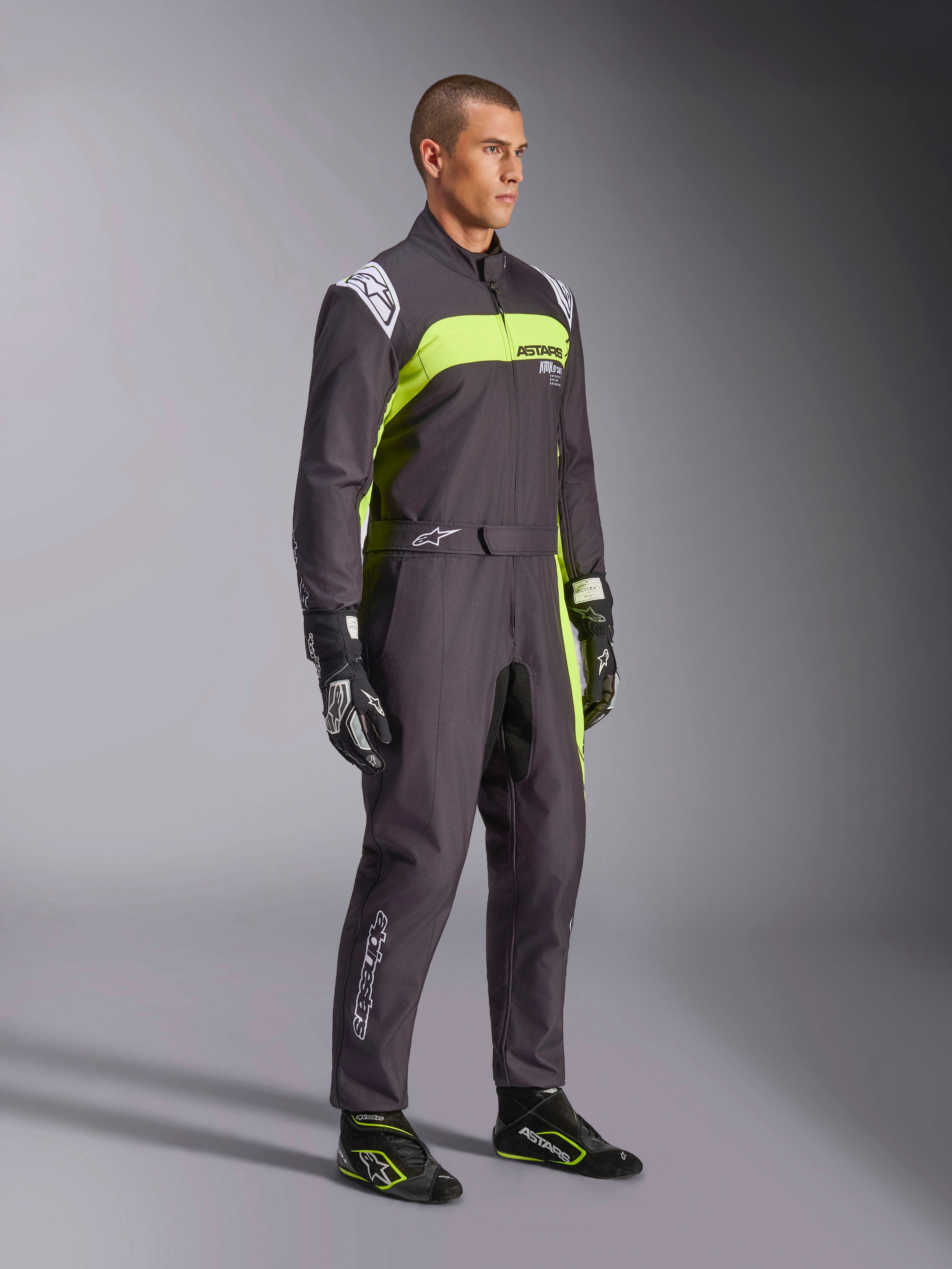 Male model wearing Alpinestars KMX-9 V3 Graphic 3 Suit in Black and Yellow Fluo, professional karting gear with vibrant neon yellow panels and white logo accents, accessorized with coordinated racing gloves and shoes, set against a studio background.