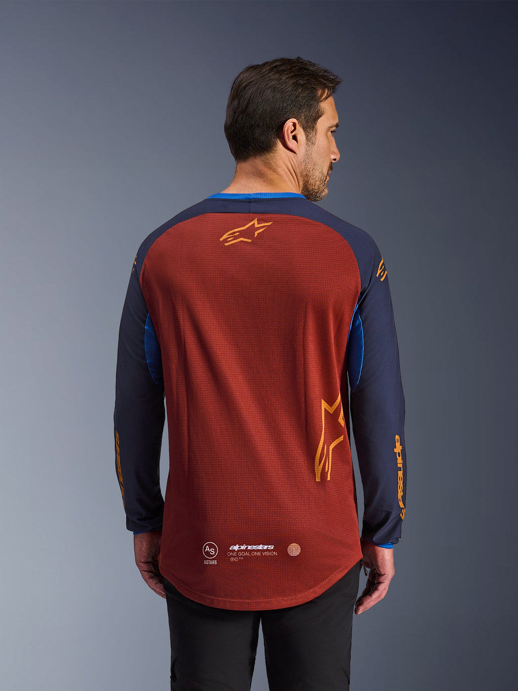 Alpinestars Maxdura Dual Trikot in Rostbraun und Mood Indigo, Rückansicht, mit einem atmungsaktiven Mesh-Torso, dunkelblauen Ärmeln mit orangefarbenem Alpinestars-Branding und einem abgesenkten Saum im Rückenbereich für zusätzliche Abdeckung.