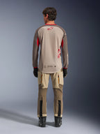 Alpinestars Maxdura Dual Jersey in Aluminum Walnut, Rückansicht, beigefarbener Mesh-Torso mit braunen Ärmeln und roten Logos, verlängerter Rückensaum, kombiniert mit Adventure-Fahrhose und schwarzen Stiefeln.