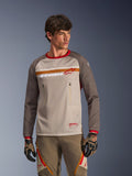 Alpinestars Maxdura Dual Jersey in Aluminum Walnut, Adventure-Motorradtrikot mit atmungsaktivem Mesh-Torso, walnussbraunen, abriebfesten Ärmeln und Brusttaschen mit Reißverschluss, getragen von einem Model mit passender Offroad-Ausrüstung.