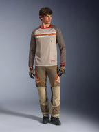 Alpinestars Maxdura Dual Trikot in Aluminum Walnut, Adventure-Motorradtrikot mit beigem Mesh-Torso und braunen Ärmeln, mit rotem Kragen und horizontalem Bruststreifen mit Alpinestars-Logo, getragen mit passender Adventure-Hose und Handschuhen.