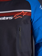 Alpinestars Maxdura Dual Jersey, Nahaufnahme von Brust und Ärmel, Dunkelgrau und Königsblau, mit Reißverschluss-Brusttasche, atmungsaktivem Mesh-Torso und integrierter Polsterung an den Ärmeln, Alpinestars-Logo auf roten und weißen Streifen.