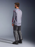 Mann im Alpinestars Maxdura Dual Jersey, hellgrau mit roten Alpinestars-Logos, Rückansicht mit Mesh-Torso und langen Ärmeln, kombiniert mit anthrazitfarbener technischer Hose und schwarzen Motorradstiefeln