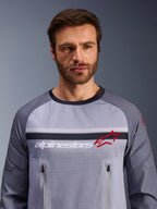 Alpinestars Maxdura Dual Jersey, Mittelgrau und Dunkelgrau, getragen von einem männlichen Model, Mesh-Torso für Belüftung, zwei Brusttaschen mit Reißverschluss, weißes „alpinestars“-Branding und rotes Stern-Logo, Performance-Offroad-Adventure-Ausrüstung