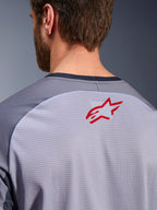 Alpinestars Maxdura Dual Jersey in Mid Gray und Dark Gray, Nahaufnahme des oberen Rückens und Kragens, mit einem kleinen roten Alpinestars Stern-Logo auf atmungsaktivem, hellgrauem Mesh-Gewebe mit dunkelgrauem Kragenbesatz, entwickelt für Adventure-Offroad-Fahrten