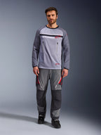 Alpinestars Maxdura Dual Jersey, Mittelgrau und Dunkelgrau, Adventure-Motorradtrikot mit Mesh-Torso und Brusttaschen mit Reißverschluss, abriebfeste Ärmel mit integrierter Polsterung, getragen mit passender grauer Performance-Hose mit roten Akzenten, technische Offroad-Fahrausrüstung