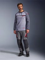 Ein Mann trägt das Alpinestars Maxdura Dual Jersey in Mittelgrau und Dunkelgrau, kombiniert mit einer farblich abgestimmten grau-schwarzen Adventure-Hose und schwarzen Stiefeln, mit atmungsaktivem Mesh-Torso, Brusttaschen mit Reißverschluss und roten Logo-Akzenten.