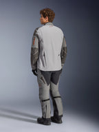 Alpinestars Nazca 3L GORE-TEX PRO Jacke, Adventure-Motorradjacke, Dunkelgrau und Mittelgrau, Rückansicht getragen mit passender Adventure-Hose und schwarzen Stiefeln, mit dunkelgrauen Superfabric-Verstärkungen an den Ärmeln, orangen Reißverschluss-Akzenten und einem kleinen roten Logo am rückseitigen Kragen.